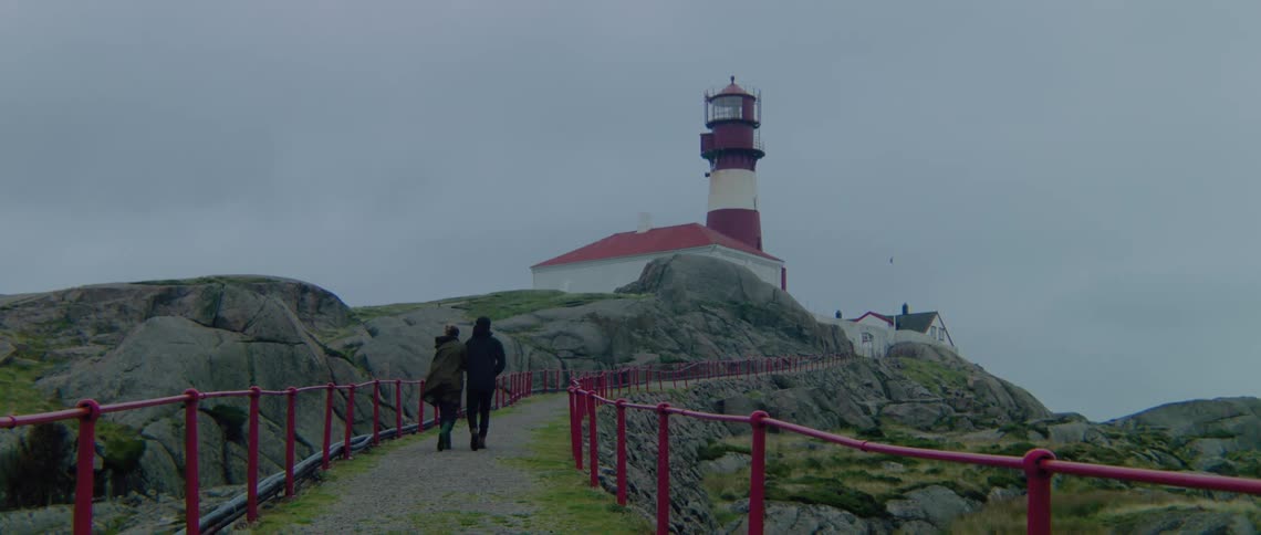 Man and woman walk up to lighthouse under the clouds