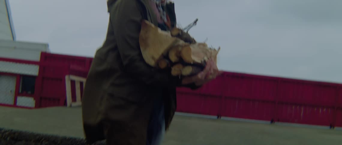 A woman walks past her home carrying chopped wood in her arms