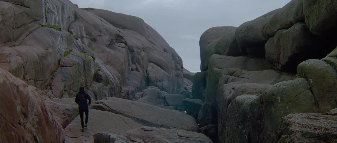 A man wearing dark clothes is jumping down mountain rocks