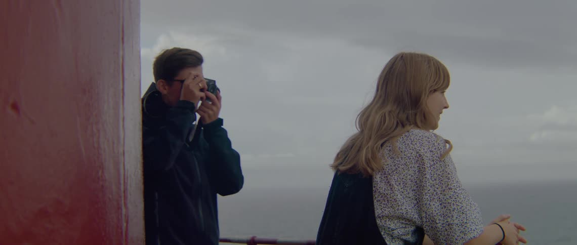 A man and a woman are looking over the side of a boat and the man is taking pictures