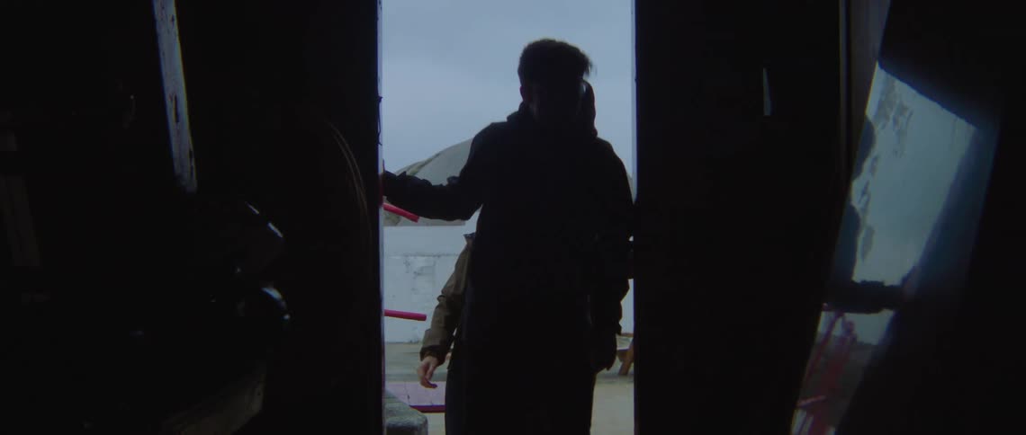 Man in black coat glasses and blonde woman enters lighthouse by red door