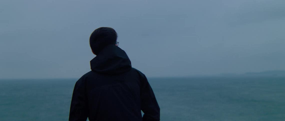 A man wearing glasses and a jacket is looking at the ocean