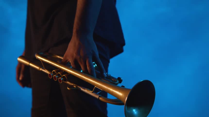 A man is standing still holding a trumpet in one hand