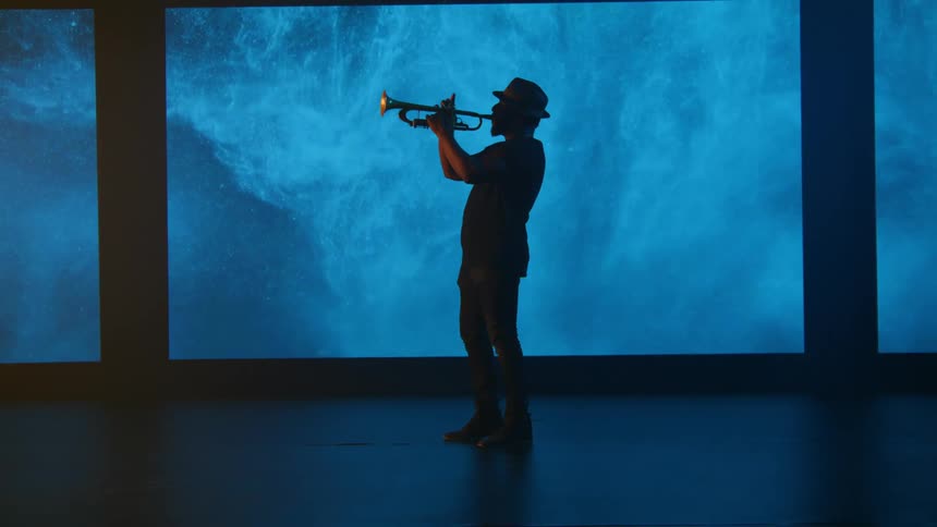 A man wearing dark clothes and a hat is playing a trumpet