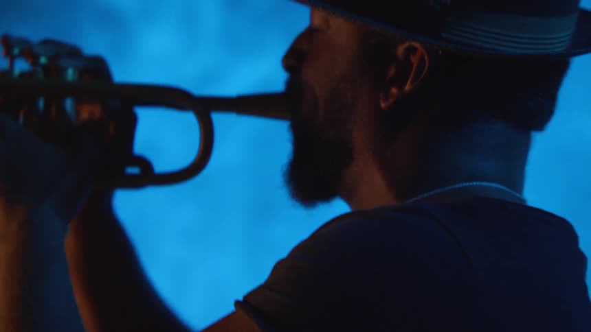 A man sways as he plays the trumpet with blue smoke as a background