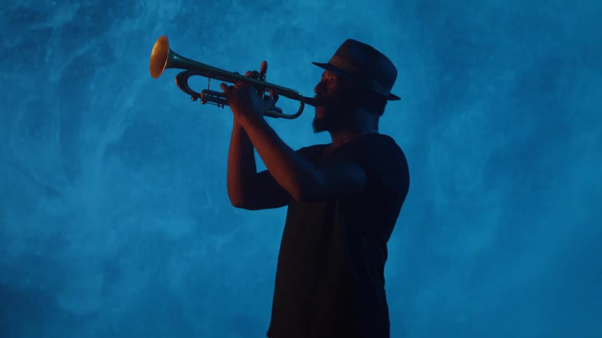 Man plays trumpet against digital wall showing blue graphic smoke