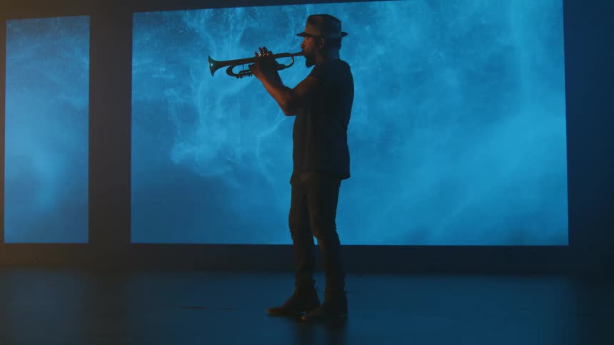A man plays the trumpet in front of a projector screen