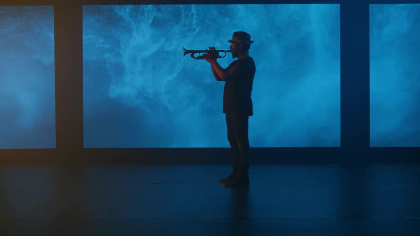 Silhouette of a trumpet musician walking onscreen who then begins to play the trumpet