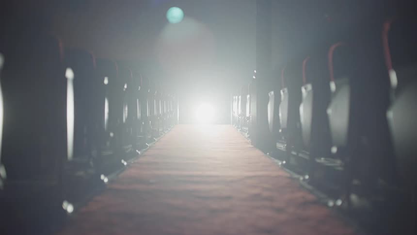 A round spotlight shines at the end of an aisle with seats on either side