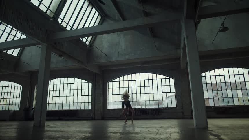 A woman dancing in a room with pillars with windows and a wall in the background