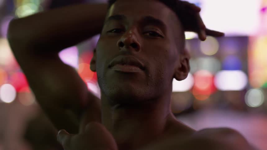 A shirtless man dances on a busy downtown sidewalk at night