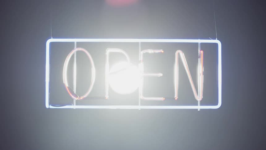 A neon sign is glowing indoors while a large spotlight behind it gets brighter until it washes out the light of the neon sign