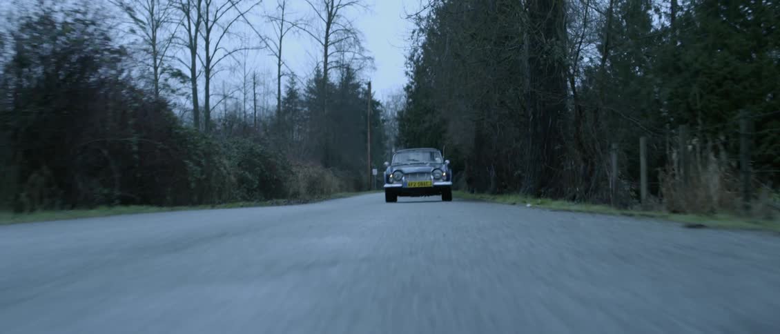 A vehicle driving on a road surrounded by trees with the sky and clouds in the background