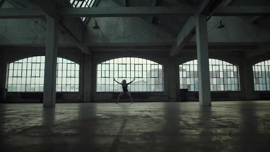Blonde woman with long hair and black dress performs ballet in spacious building