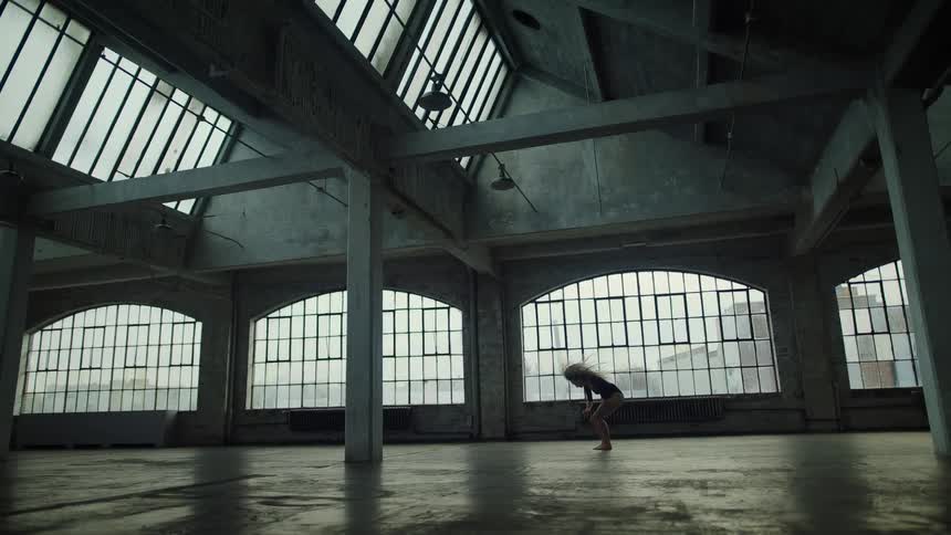 A woman dancing in a room with pillars with windows and a wall in the background