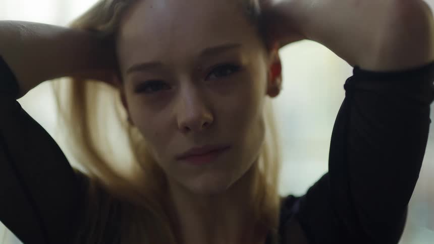 A blond haired woman pulls her hair up over her head with both hands