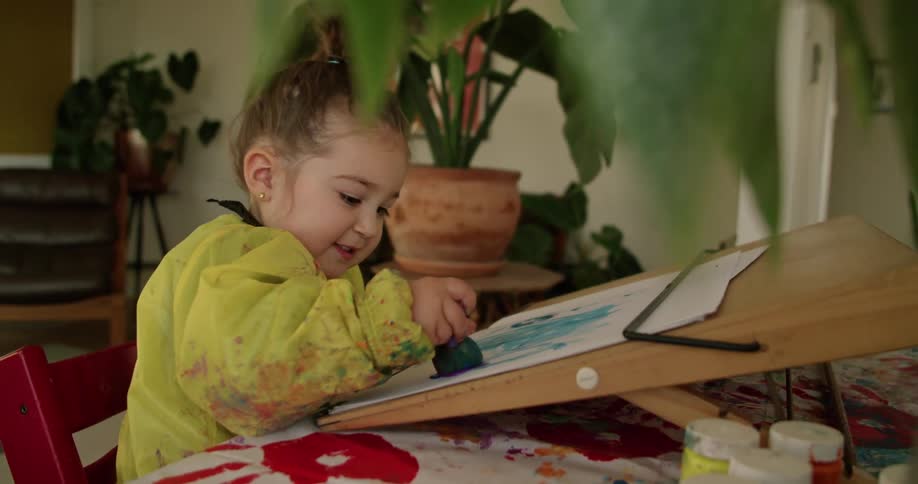 A little girl is smiling as she is painting on paper with a sponge brush