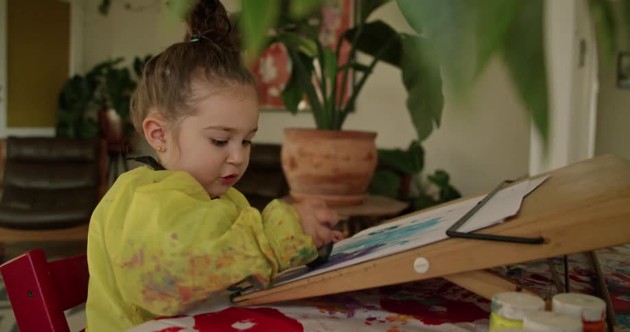 A toddler is painting on paper with a sponge brush