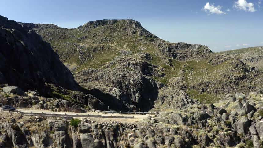 A car travels on a narrow road along a mountain ridge