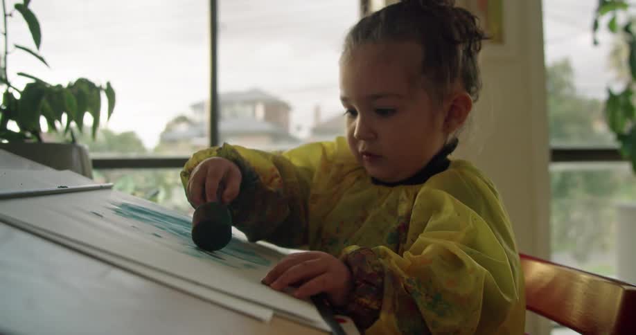 A baby is painting on a paper on the desk