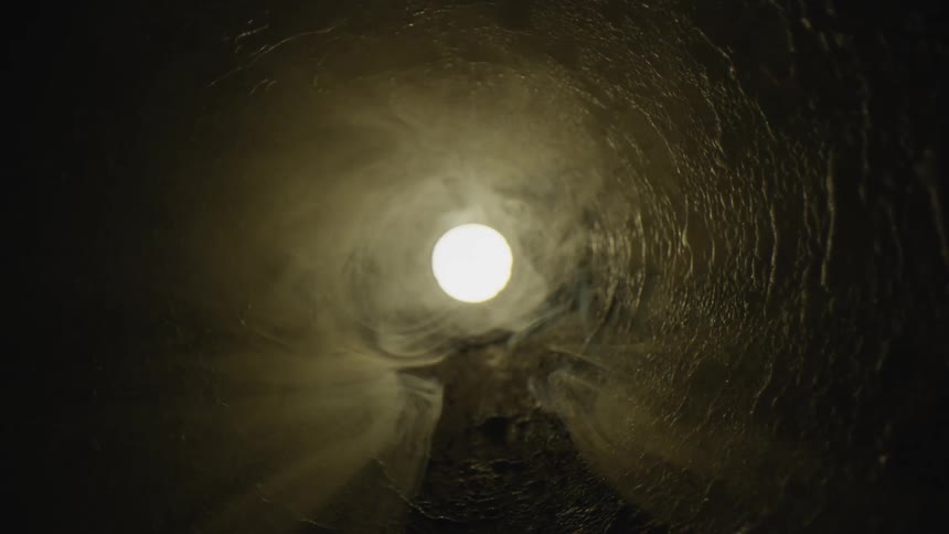 Misty smoke floats in the air of a tunnel with a perfect circle of light at the end