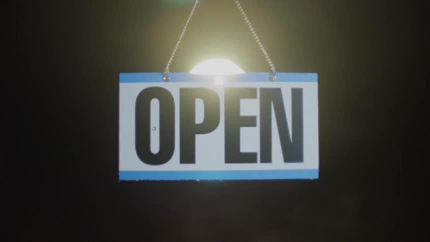 A spotlight shines behind a hanging open sign