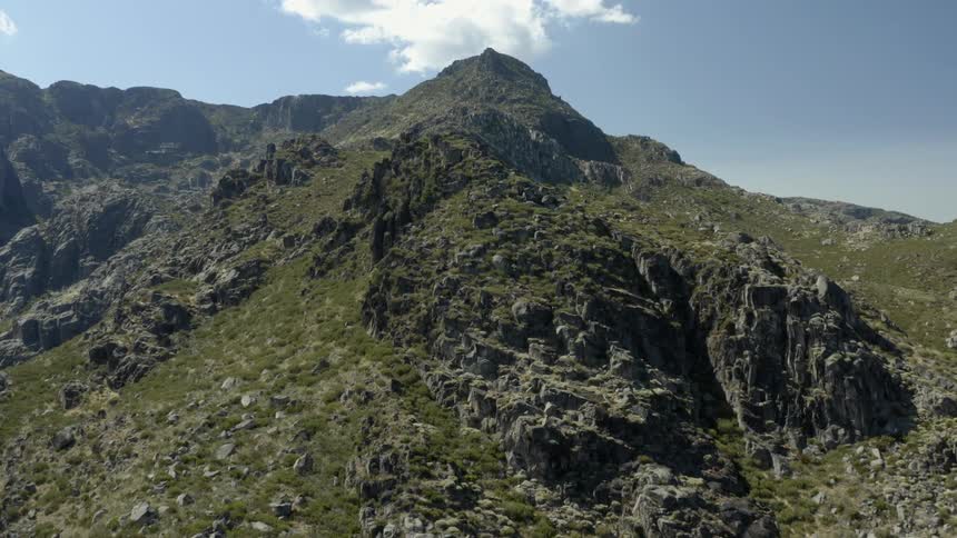 Grass and plants are growing on a rocky mountain ridge high in a cloudy sky
