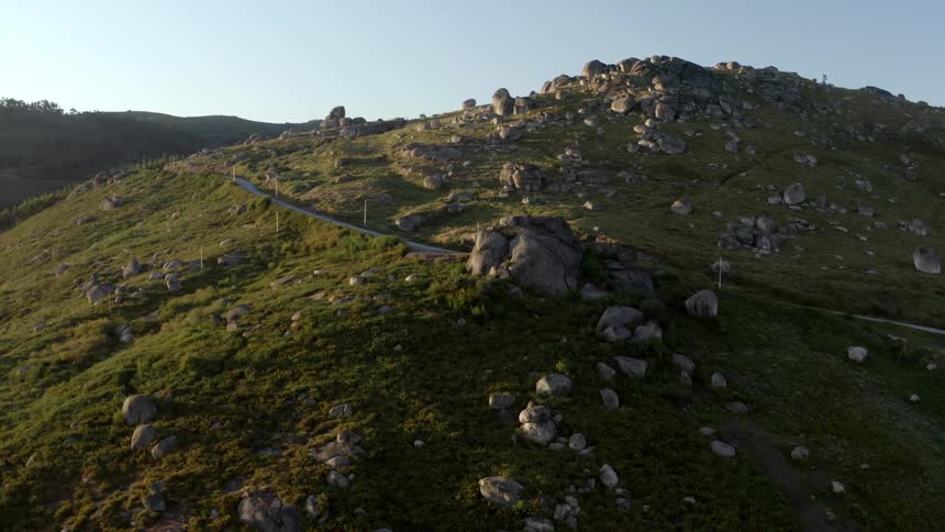A road on a grassy hill with rocks with the sky and clouds in the background