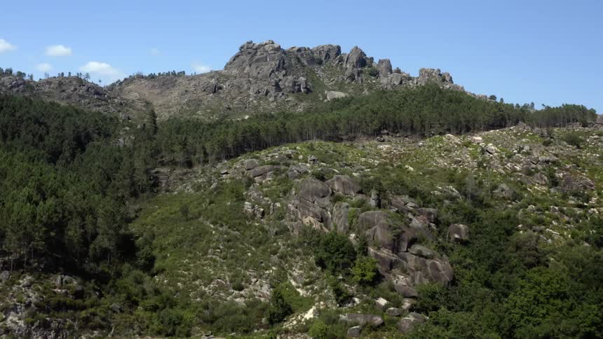 Cars travel on a road through forested mountains and there is a mountain ridge high in the sky