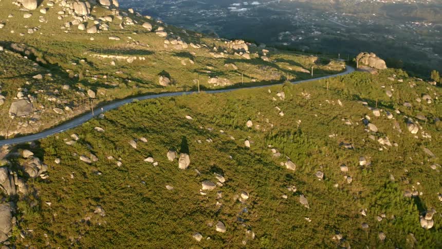 A road runs through the side of a tall hill dotted with large boulders