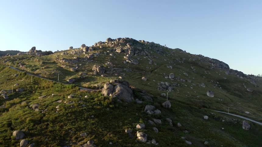 A road on a grassy hill with rocks with the sky and clouds in the background