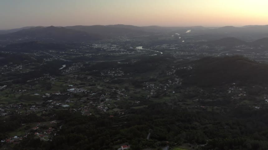 An aerial view of a small town on a hilly landscape with mountains and a river at dawn