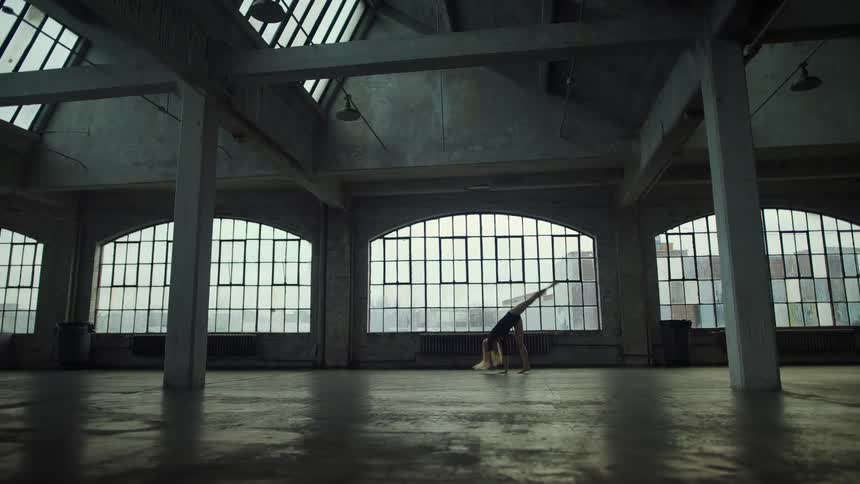 Blonde woman with long hair and black dress performs ballet in spacious building