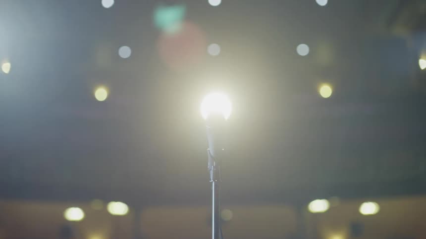 Bright lights turn on in a room with stadium seating and a microphone