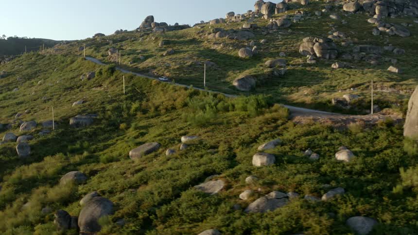 A car travels on a road around a mountain covered in rocks and boulders