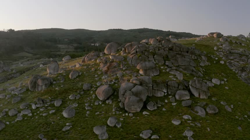 An aerial view of a hillside with large rocks on it in a rural area with buildings in the background