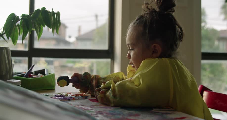 A young girl dips a sponge into a pile of paint spread across a table