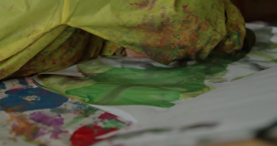 A young girl wears a smock as she using a rolling sponge to smear paint on a large piece of paper