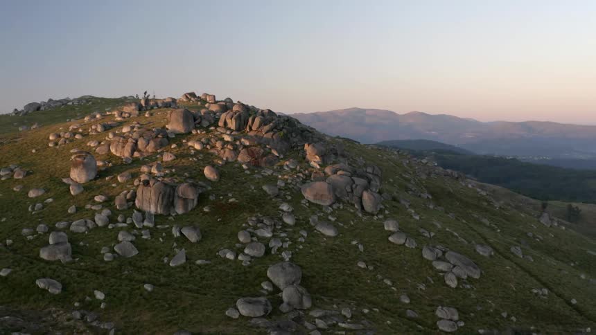 A hill with rocks with a mountain range the sky and clouds in the background