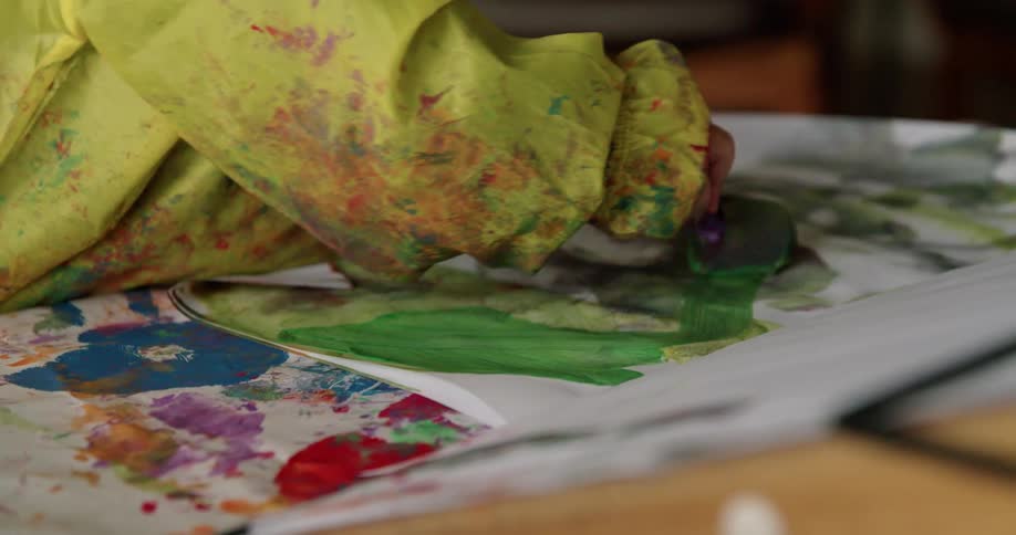 A little girl is painting on paper at a table inside a home during the daytime