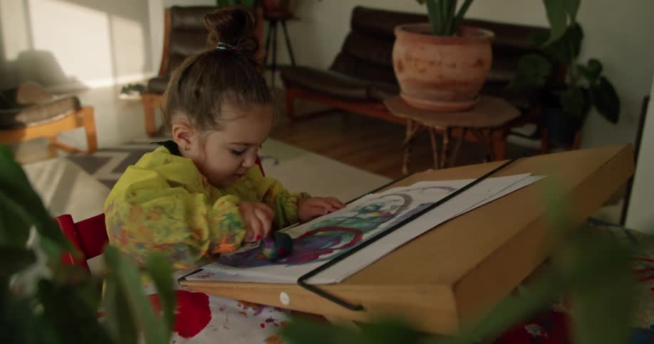 A child is sitting in a red chair and painting on paper with a sponge brush