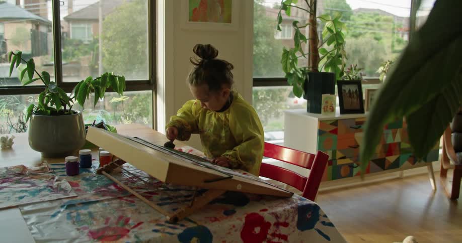 A little girl uses a sponge brush to paint on a tabletop easel