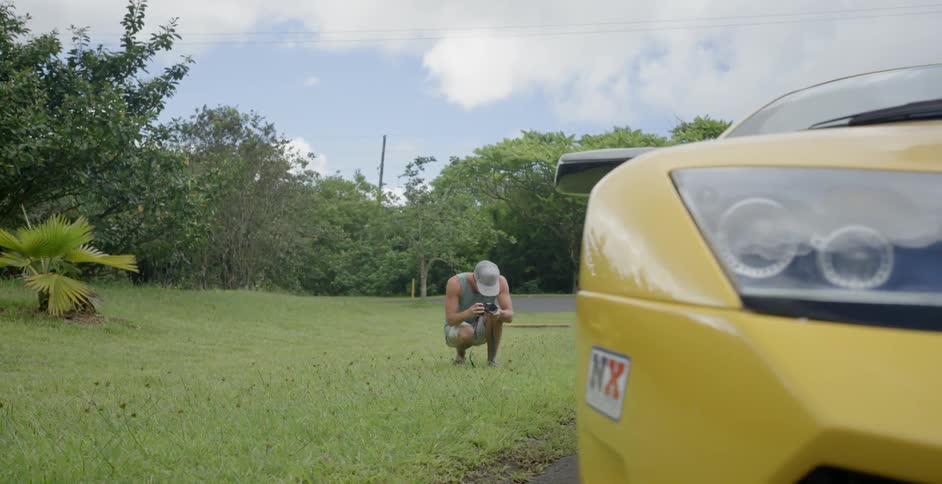 A man crouches in the grass near a car
