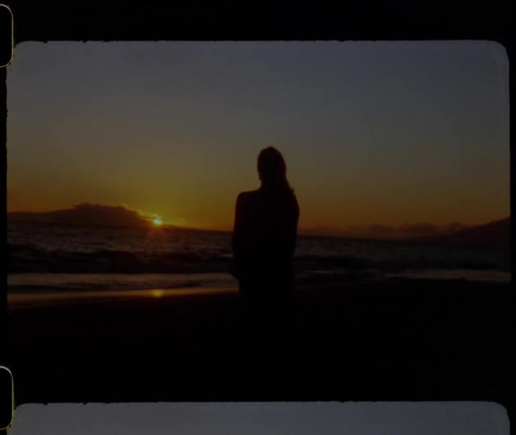 Silhouette of a woman standing on a beach and watching the sun set over a mountain