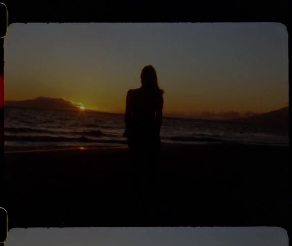 Silhouette of a person on a beach watching the sun set over a mountain