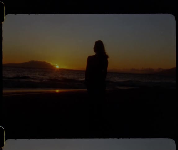 A woman watches the sun set on the beach
