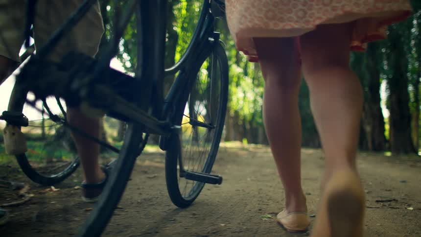 A man an woman walk their bikes along a dirt path in a forest
