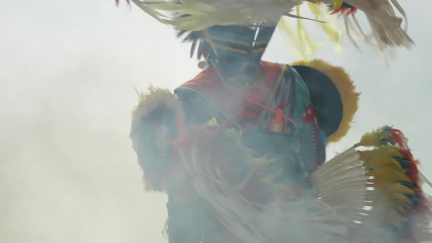 A man with traditional native american clothing dancing surrounded by smoke
