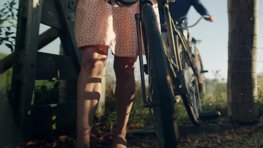 A man and a woman are walking their bicycles through a wooden gate on farmland during the daytime