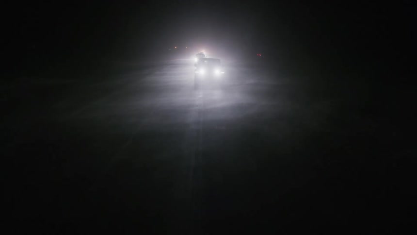 Cars with bright headlights traveling on a dark road during a snowstorm